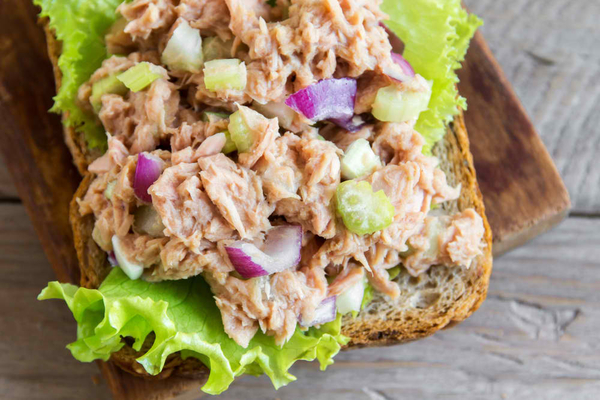 Tuna salad sandwich over wooden background, close up. Homemade sandwich with tuna and vegetables for snack.
