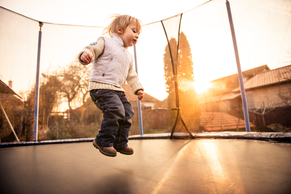 Little child jumping on big garden trampoline at sunset